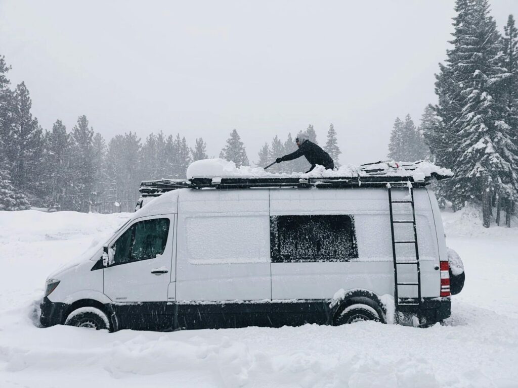 Van covered in snow with person clearing roof in heavy snowfall