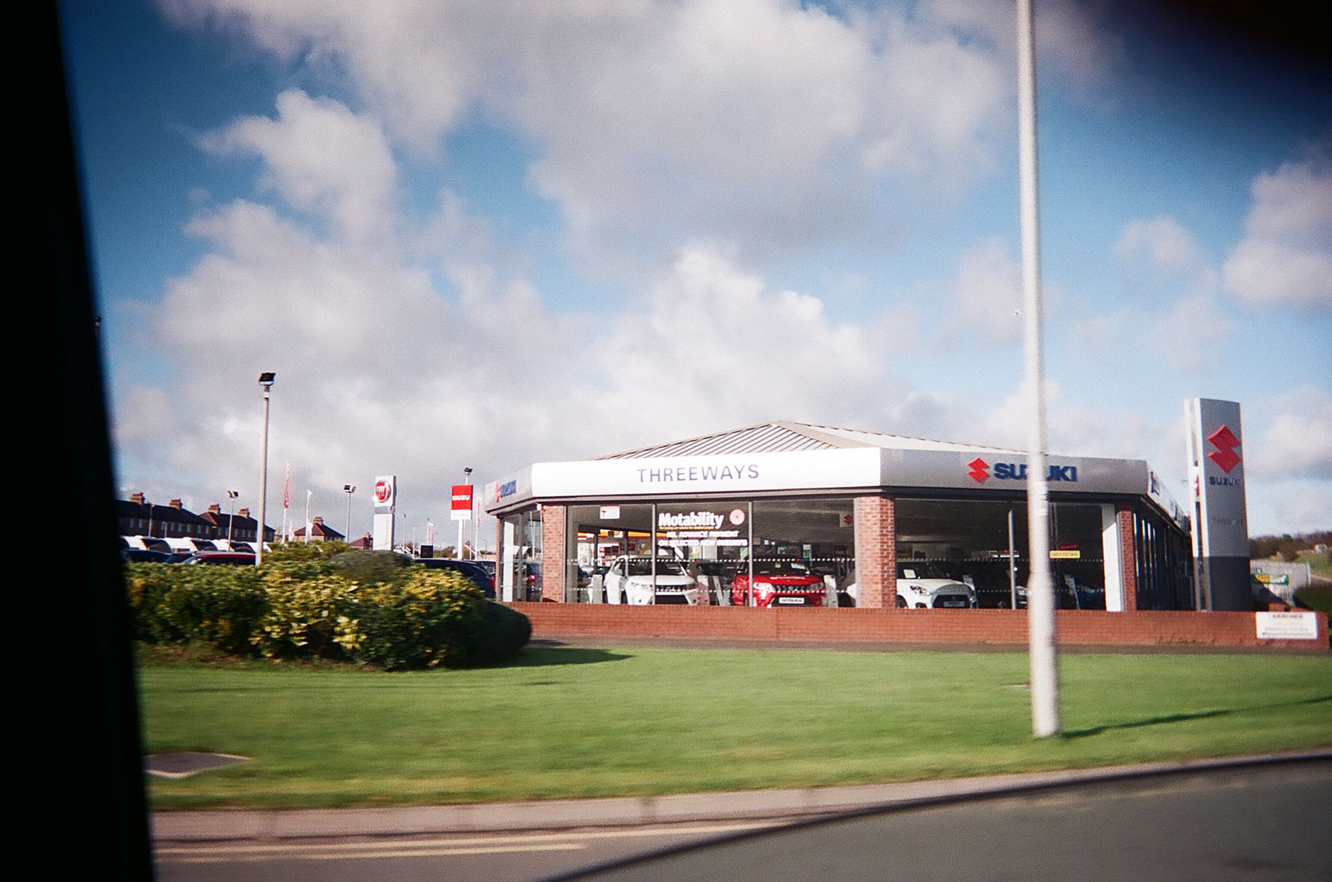 A used vehicle dealership frontage on a British street with Motability signage in the window