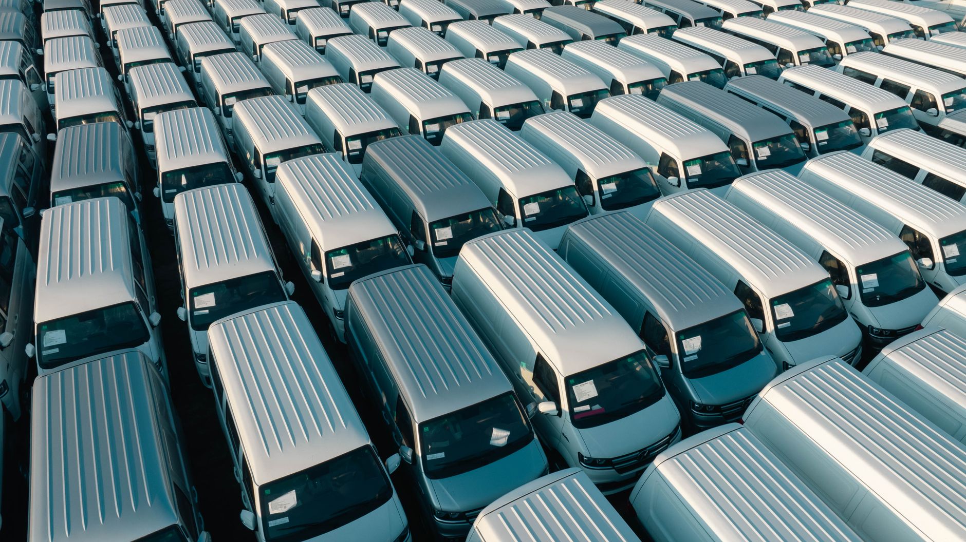 Aerial view of rows of white panel vans parked in a dealer stock compound