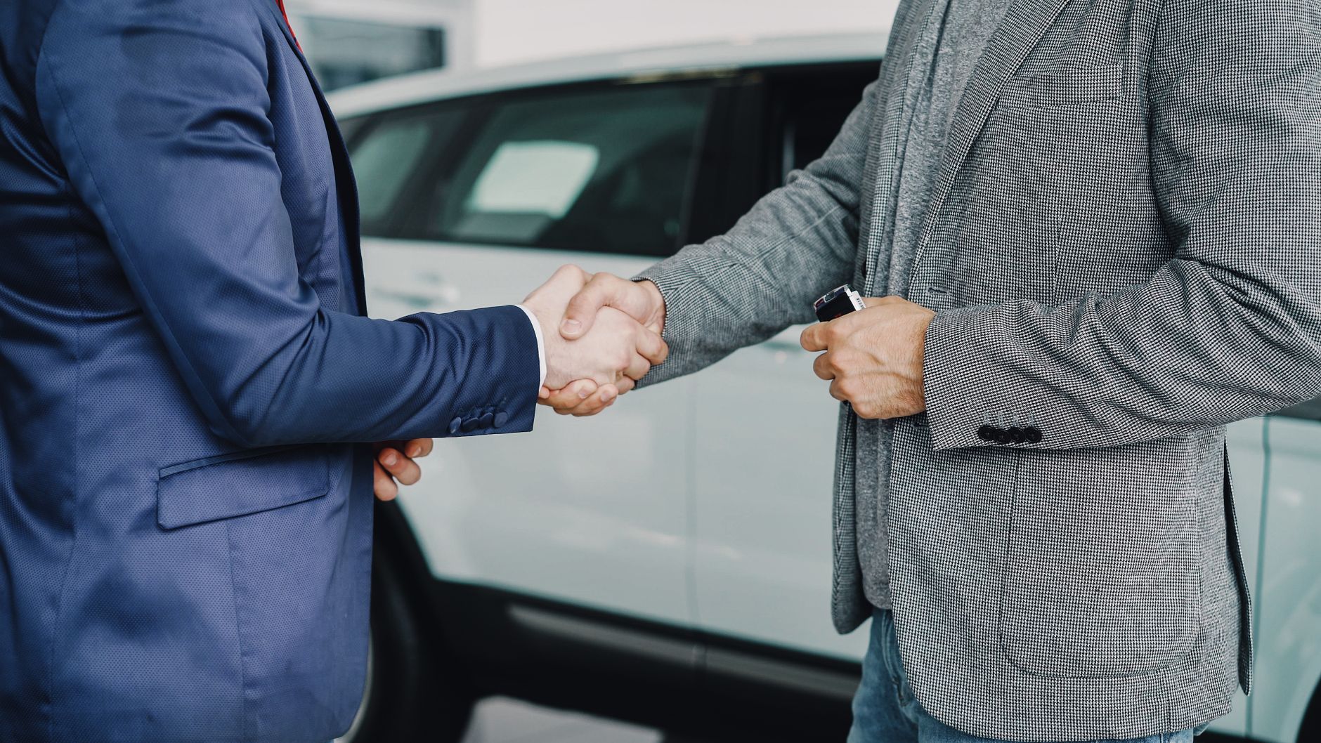 Two people shaking hands inside a vehicle dealership after agreeing a sale