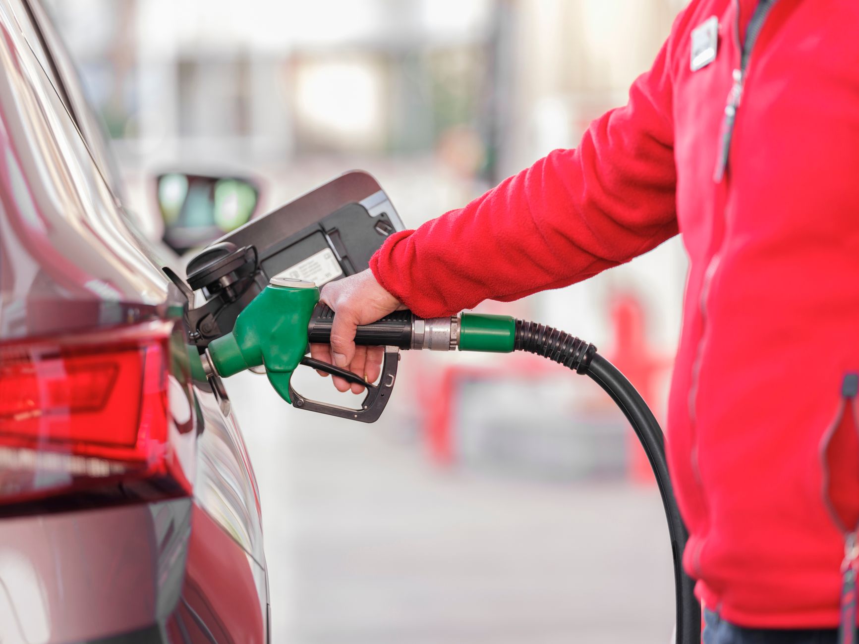 Person in a red hooded top refuelling a vehicle at a petrol station pump