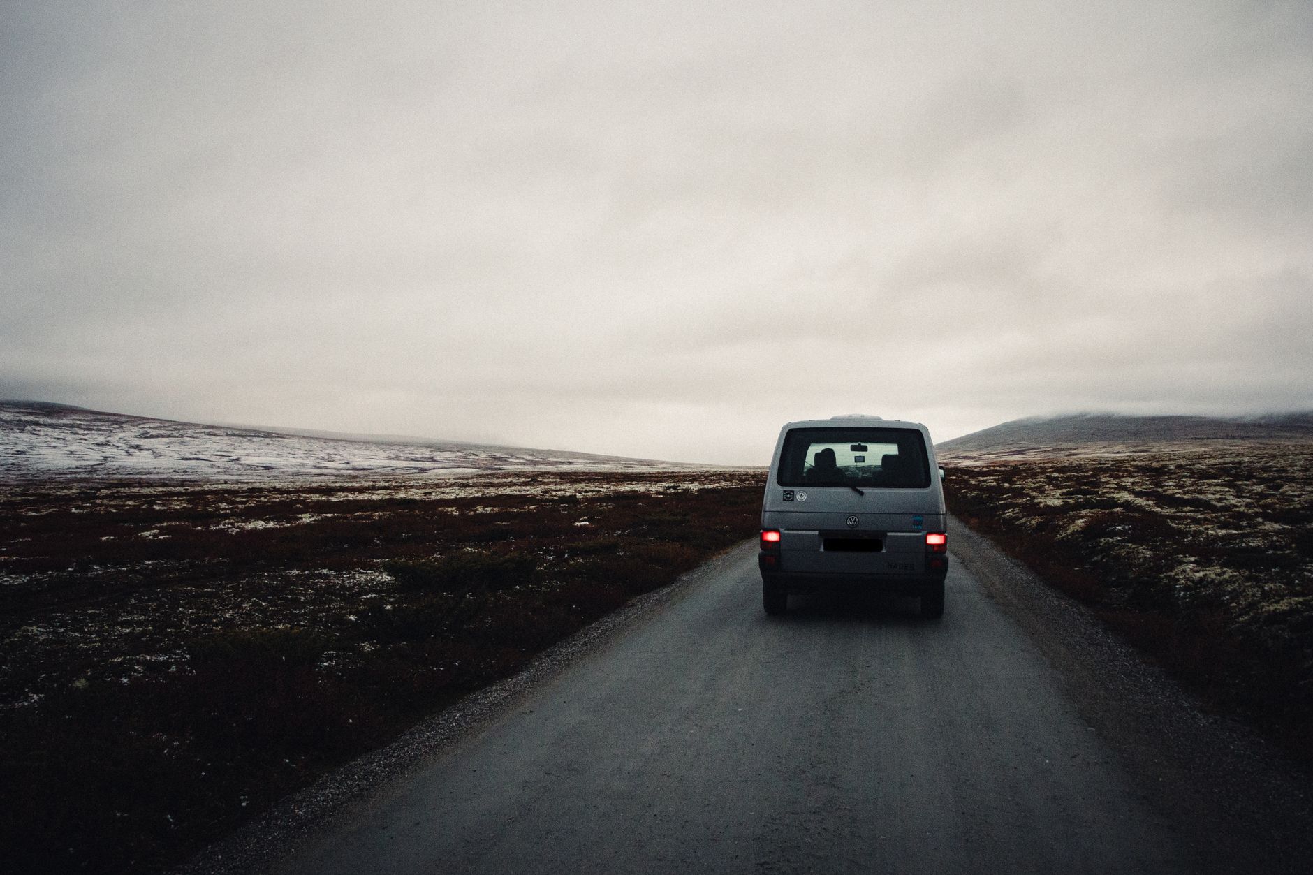 Dark panel van driving away along a misty road, seen from behind at a distance