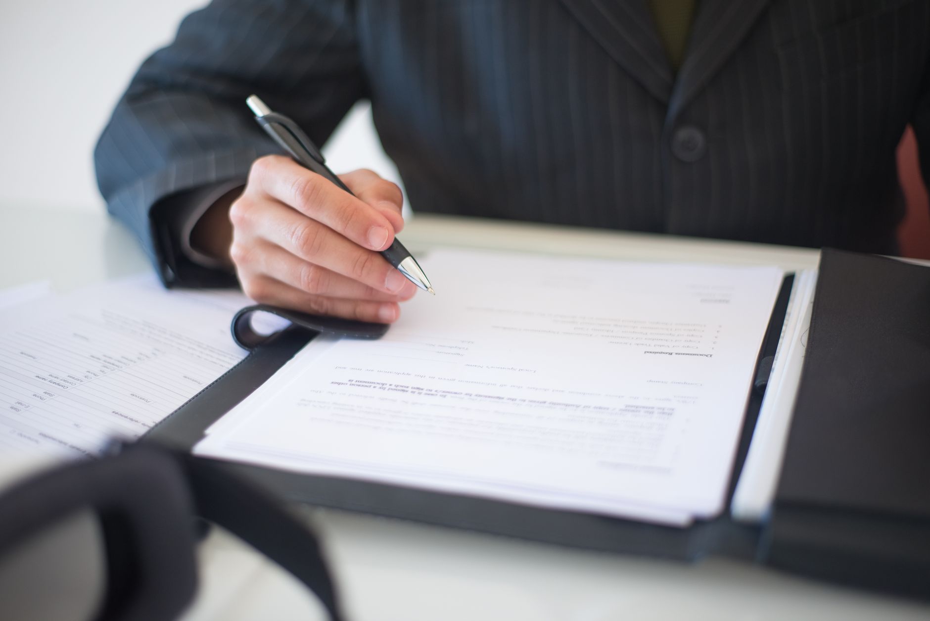 Hand signing paperwork at a desk with a calculator alongside