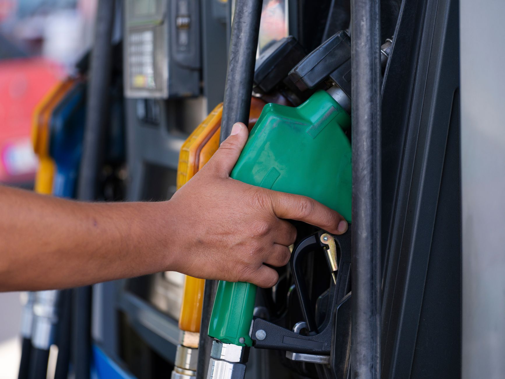 A close-up of a hand holding a fuel nozzle at a filling station pump
