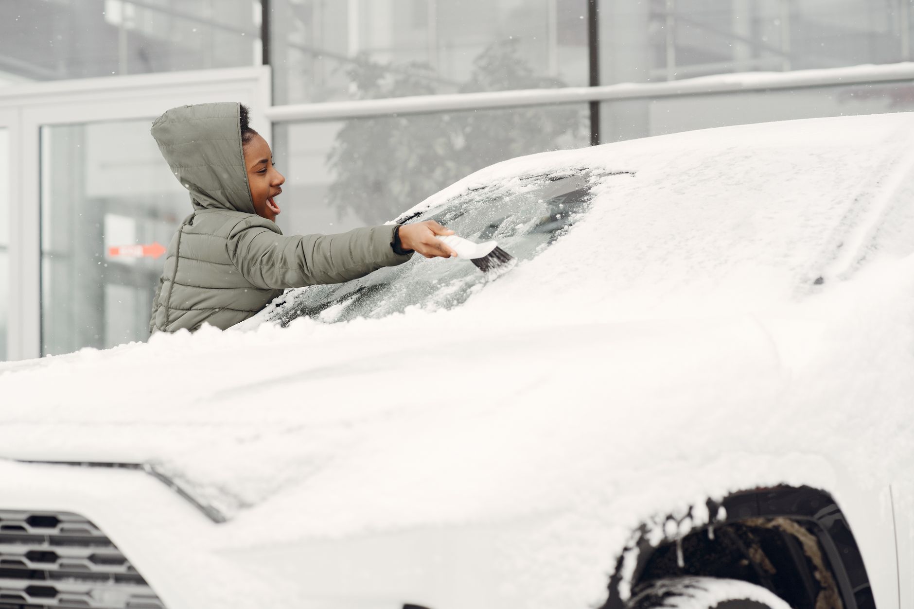 A person in winter clothing clearing snow and frost from a vehicle windscreen