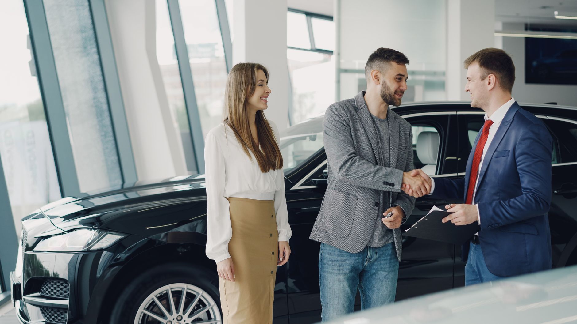 A salesperson shaking hands with a customer beside a vehicle at a dealership