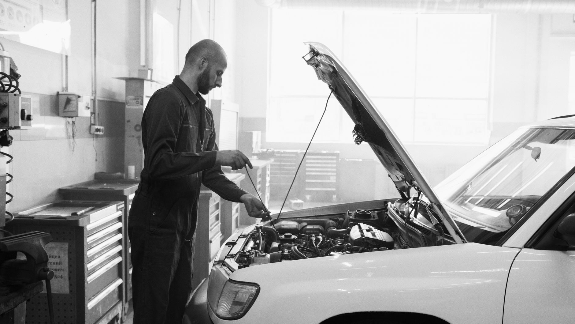 A mechanic in overalls checking the engine bay of a vehicle with the bonnet open