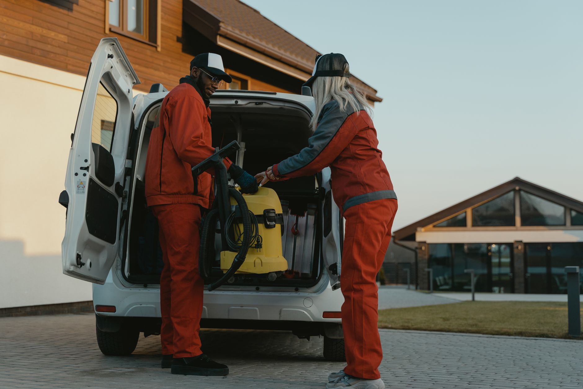 Two cleaners lifting a vacuum cleaner into the side door of a small works van