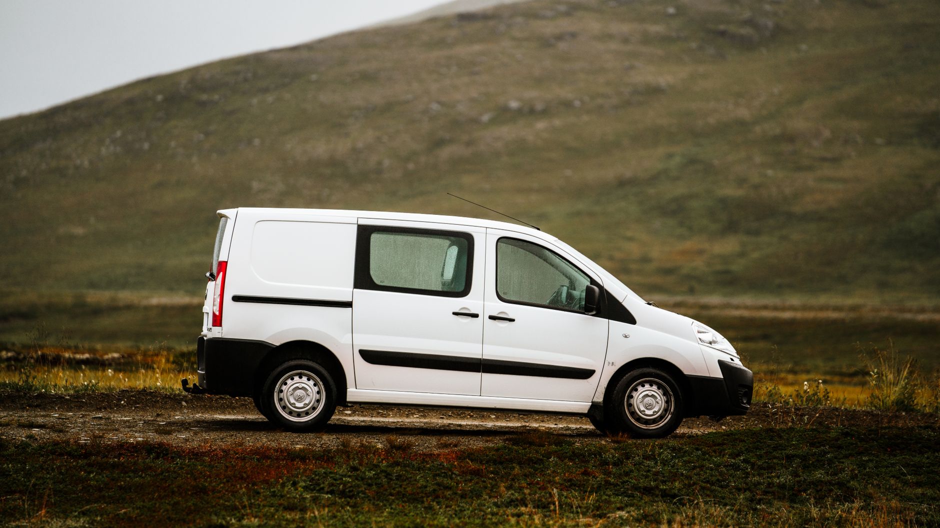 Plain white panel van parked on a quiet rural road with green hills behind