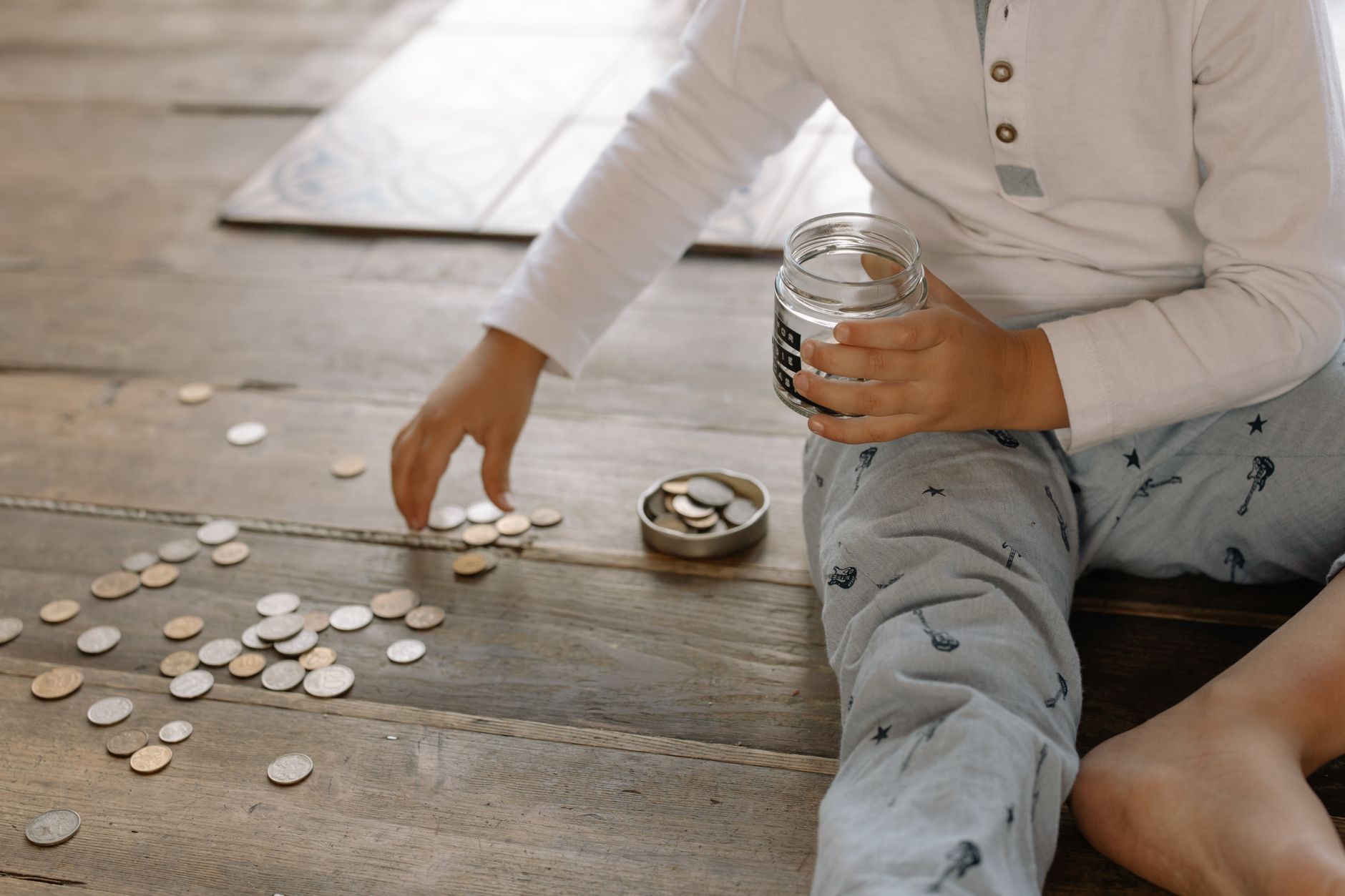 Coins being dropped into a glass savings jar on a kitchen table