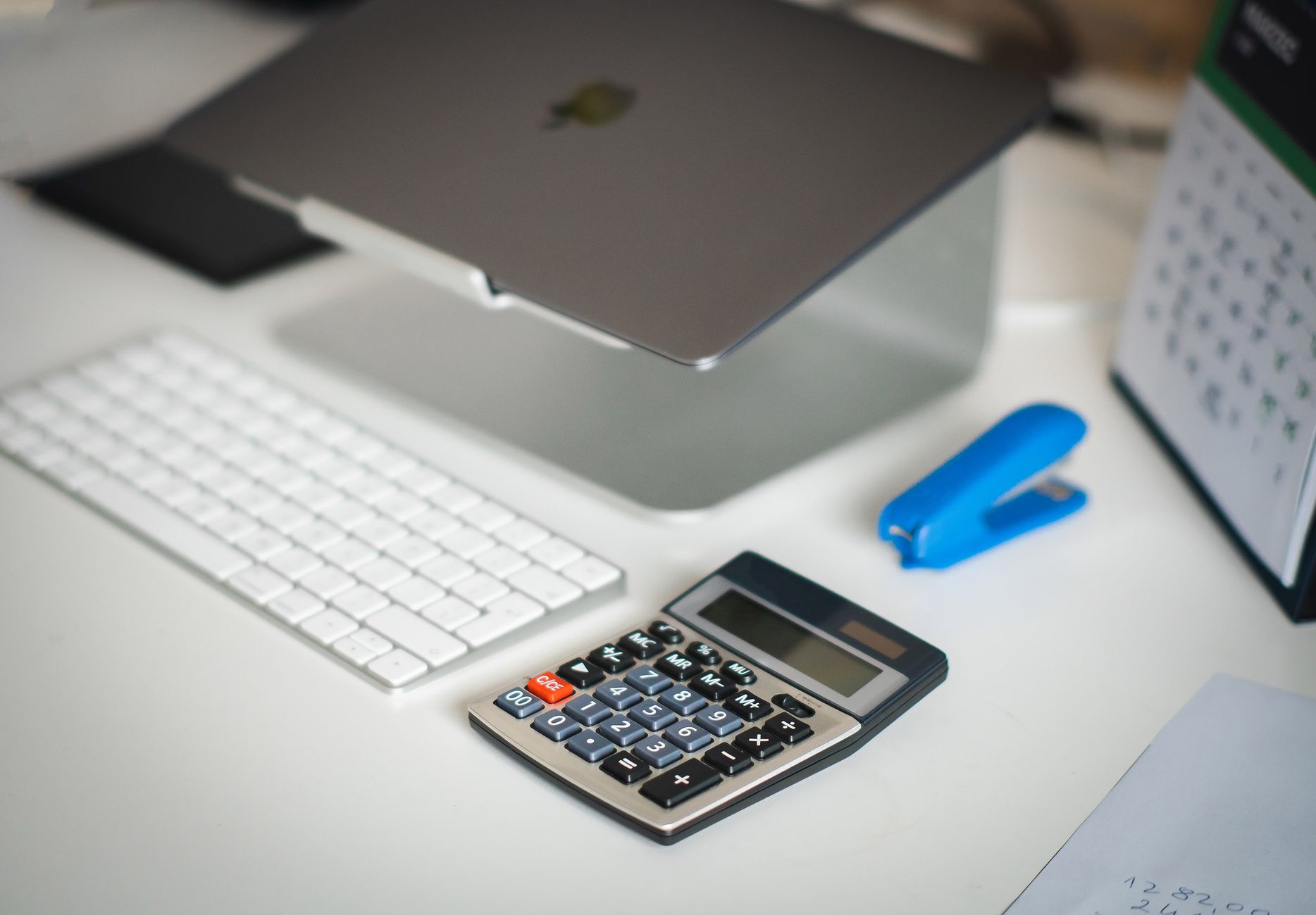 Desk with a laptop, calculator and notepad set out for working through figures
