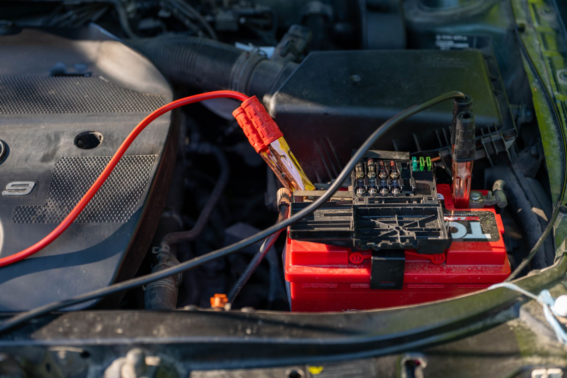 Close-up of a vehicle battery in an engine bay with red and black jump leads attached