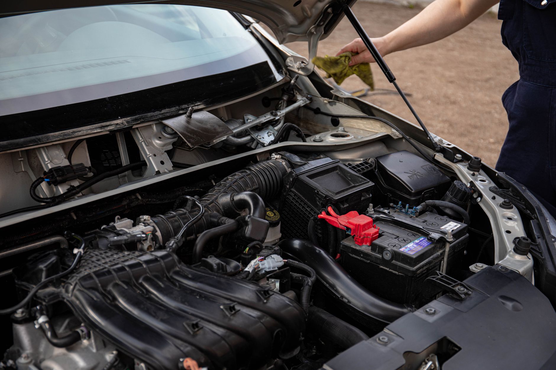 Mechanic inspecting an open engine bay and battery during a routine vehicle check