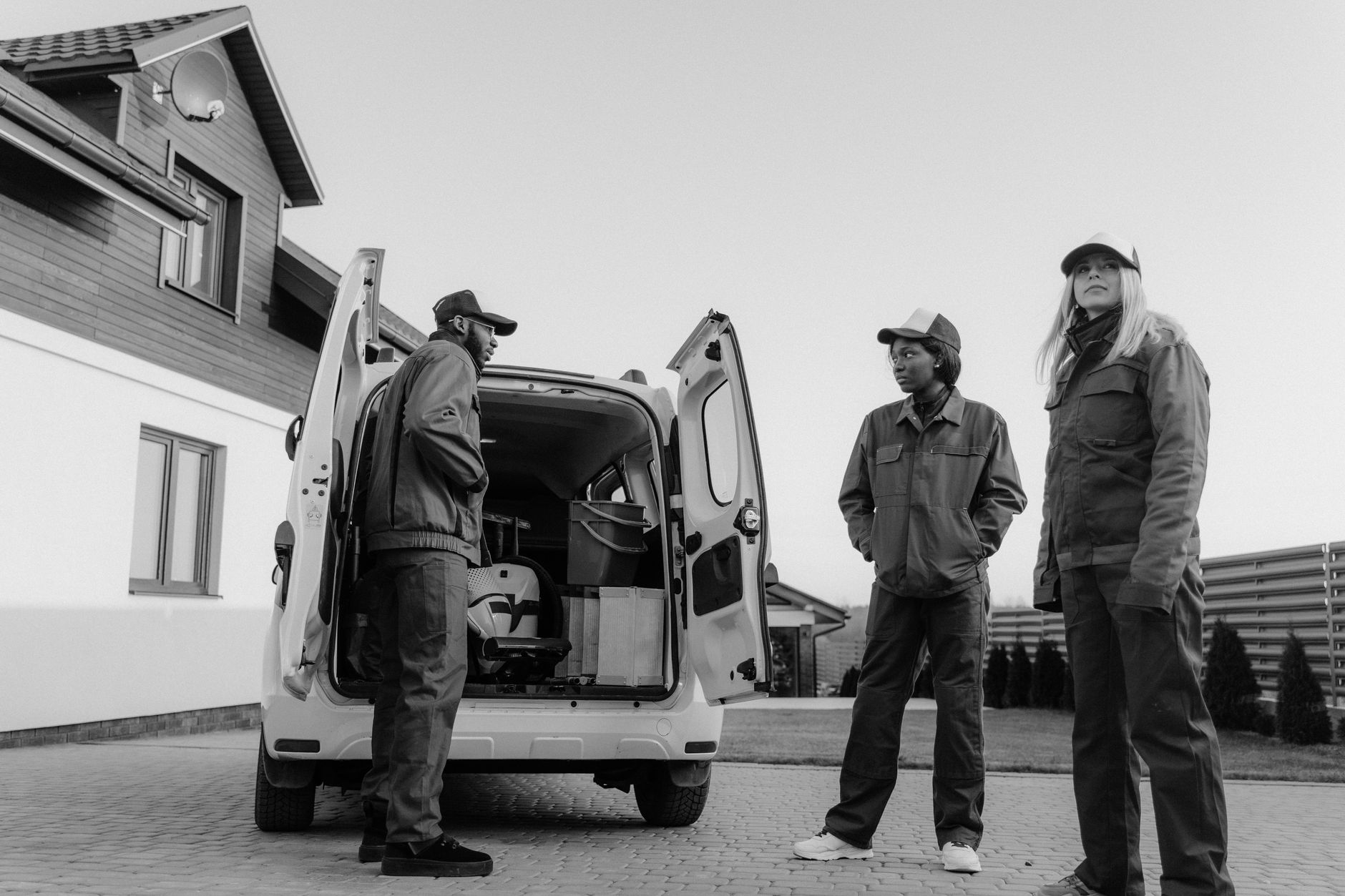 Three workers in overalls unloading tools and equipment from the rear of a van