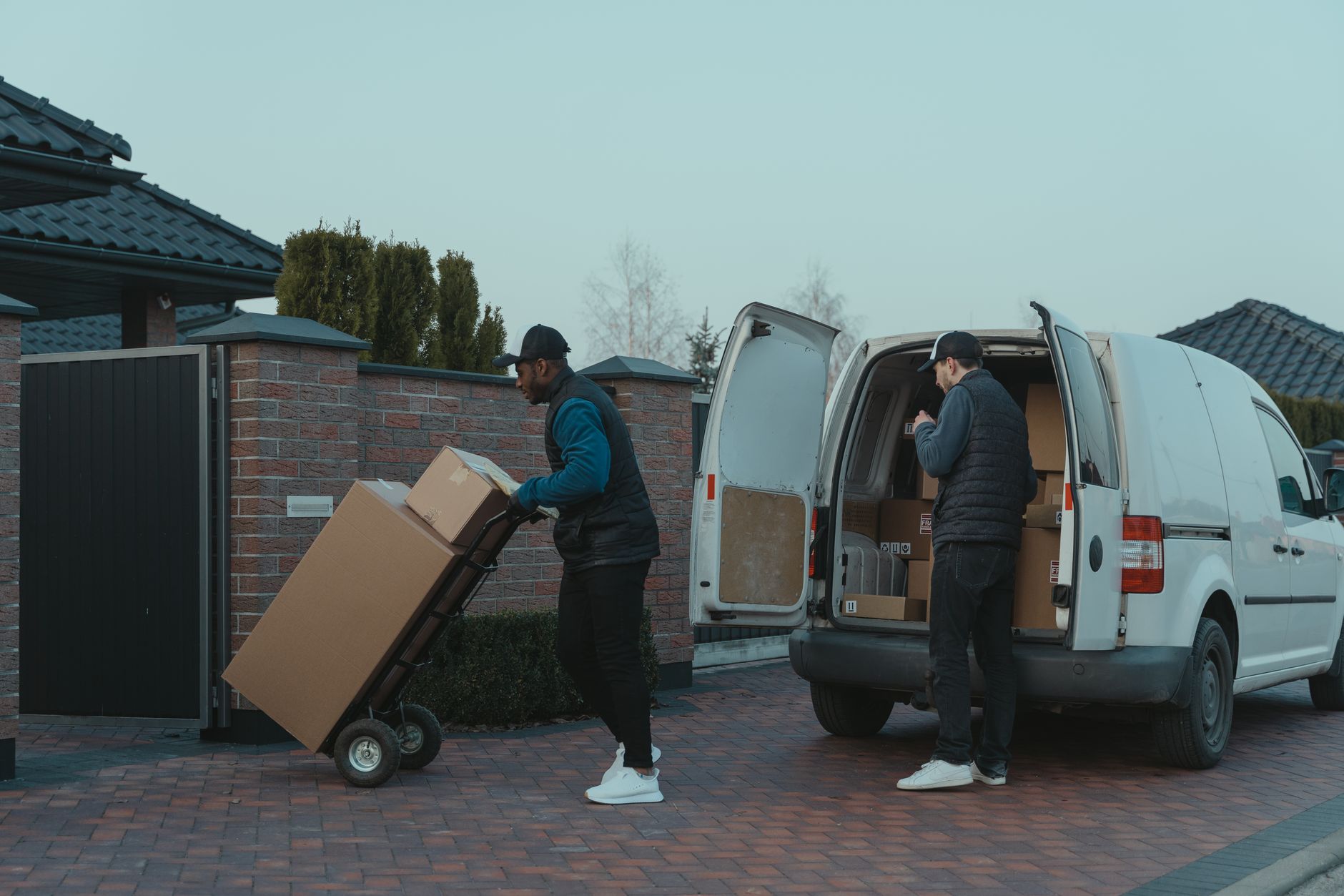 Two workers loading a parcel through the open rear doors of a small delivery van