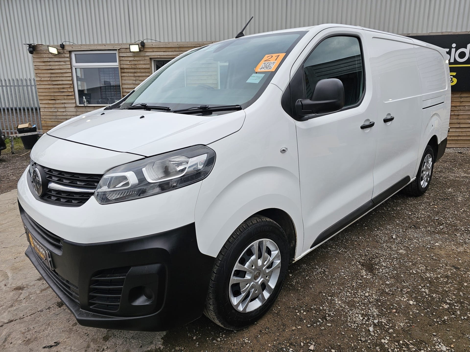 A white long-wheelbase Vauxhall Vivaro panel van seen from the front nearside on a forecourt