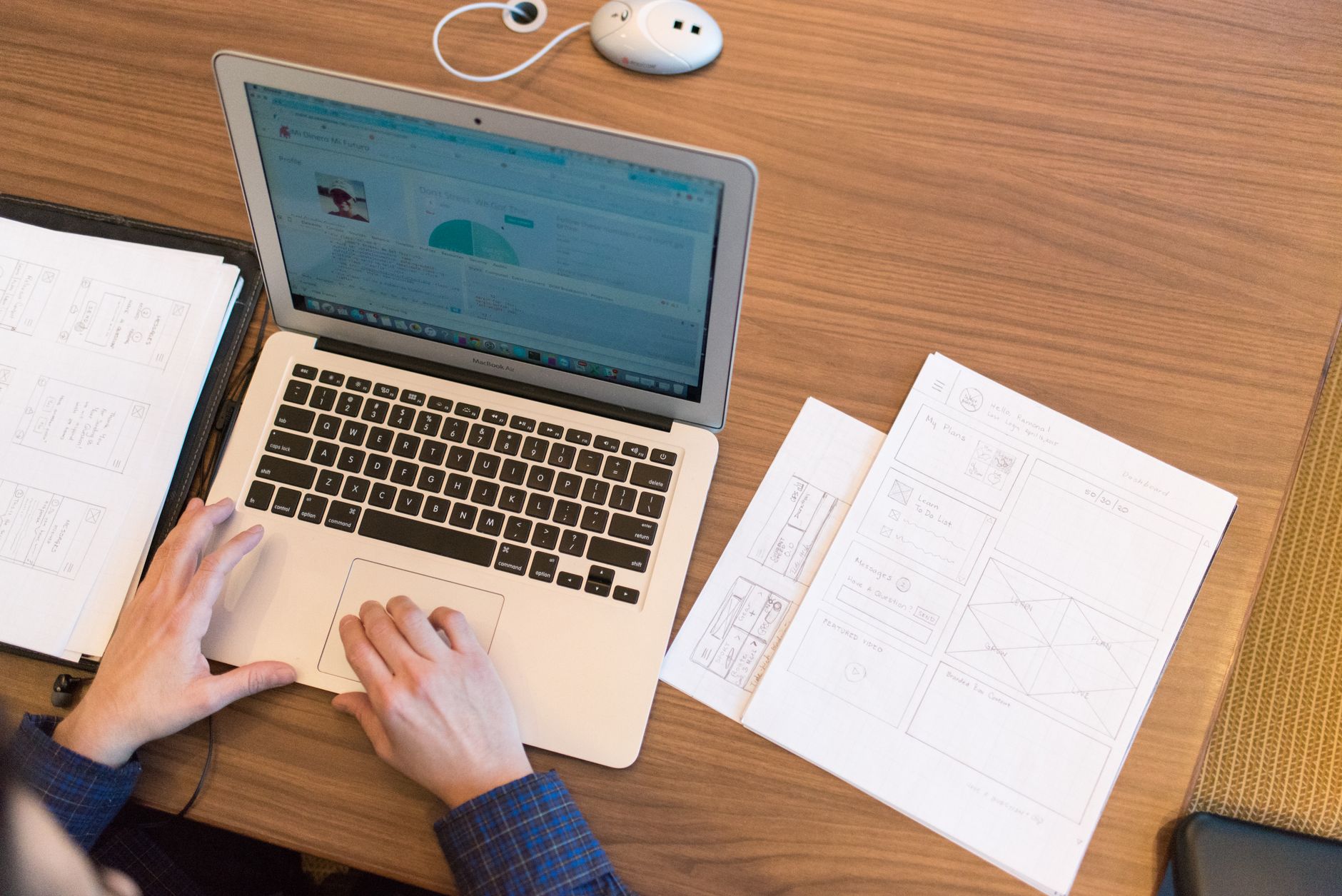A laptop, notebook and papers on a desk with hands typing an advert