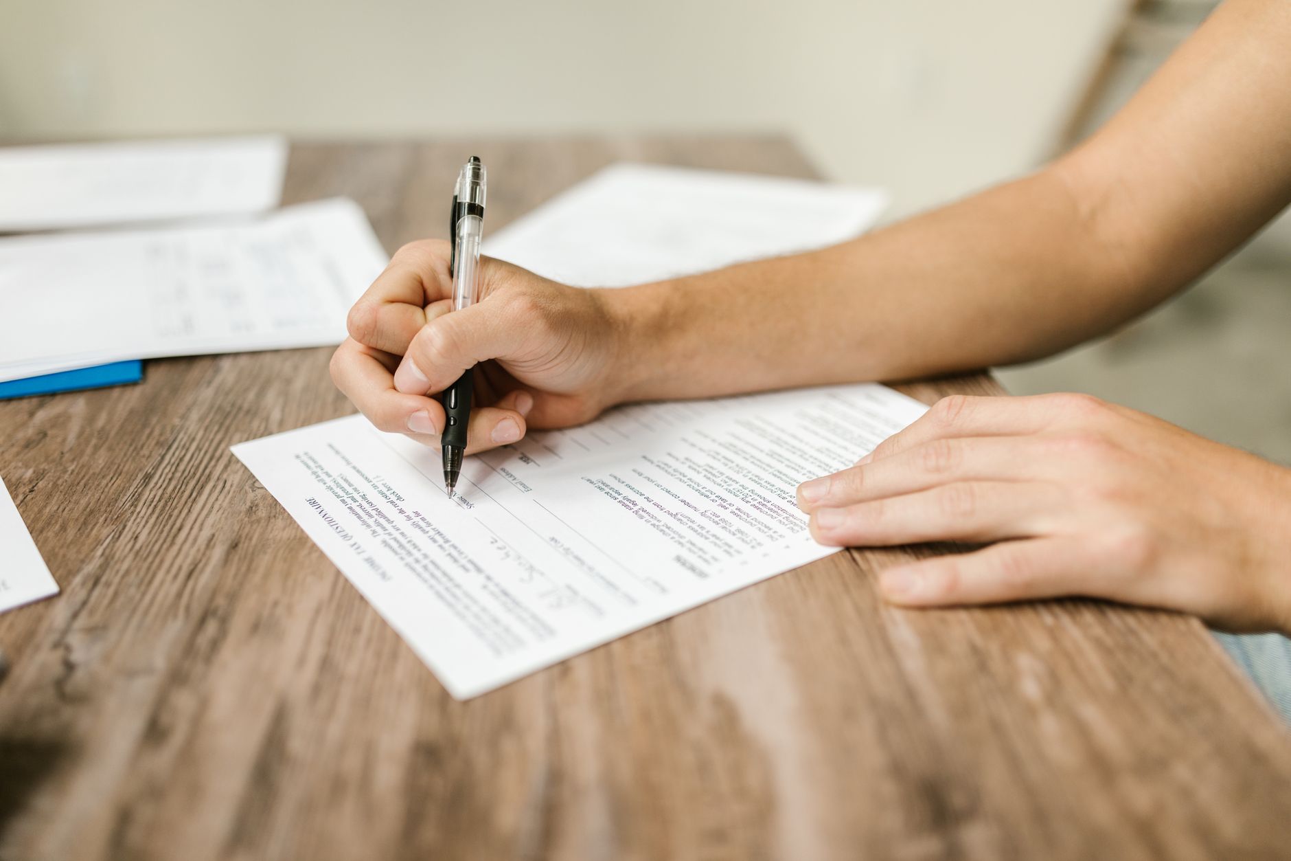 A hand signing a printed form on a wooden desk