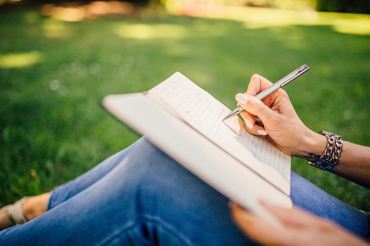 Someone writing in a notebook resting on their lap outdoors