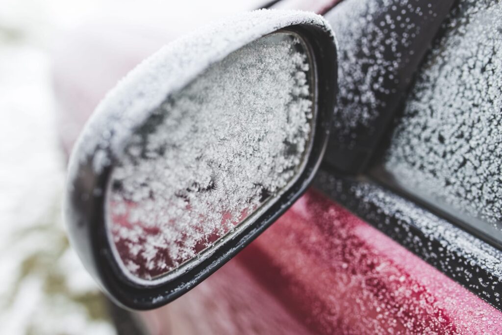 A vehicle wing mirror thickly covered in frost on a cold morning