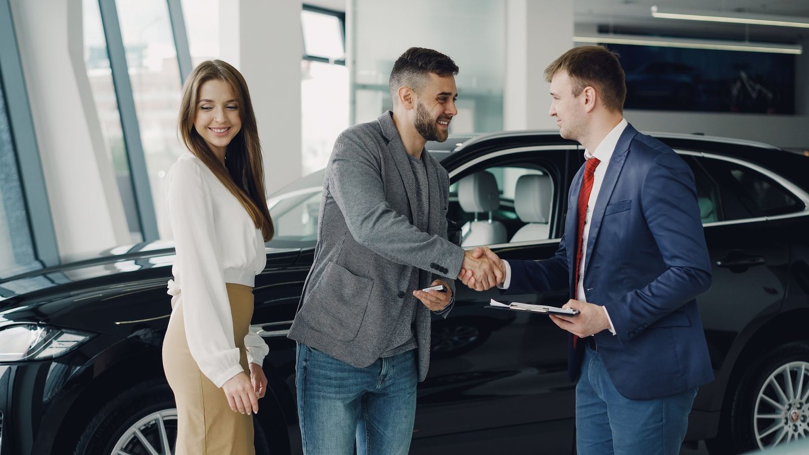 A handshake between a buyer and a salesperson beside a vehicle indoors