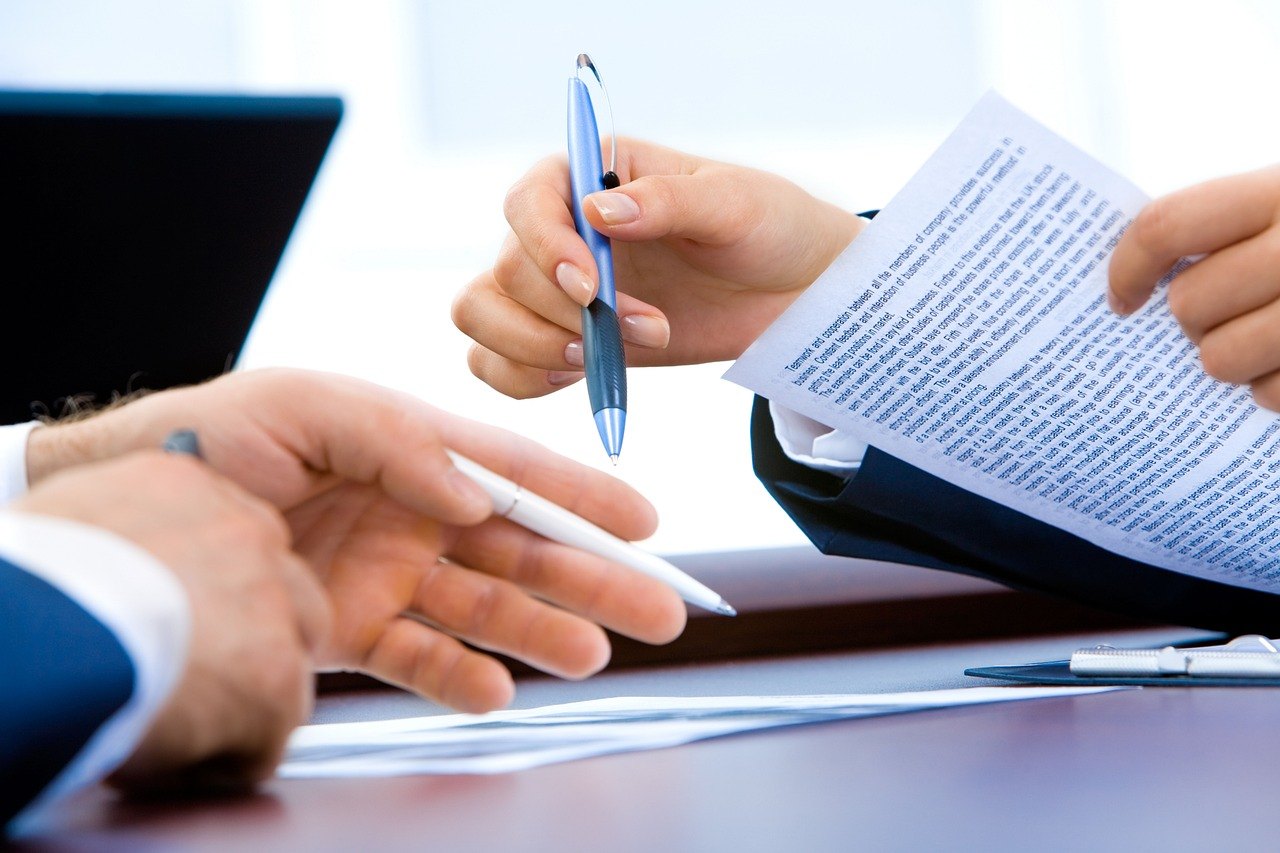 One person passing a printed document and pen to another across a desk