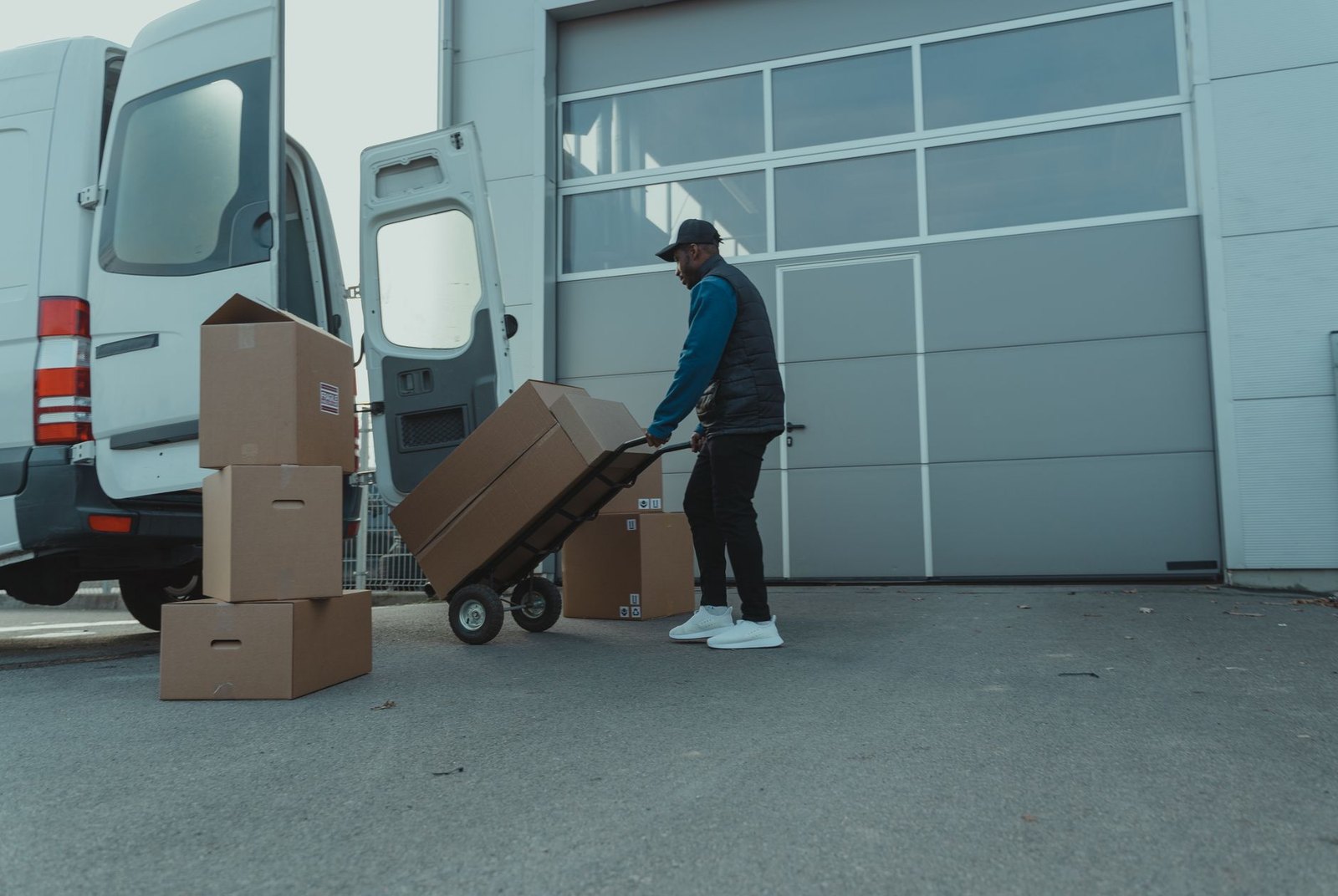 A courier wheeling boxes on a sack truck beside an open van