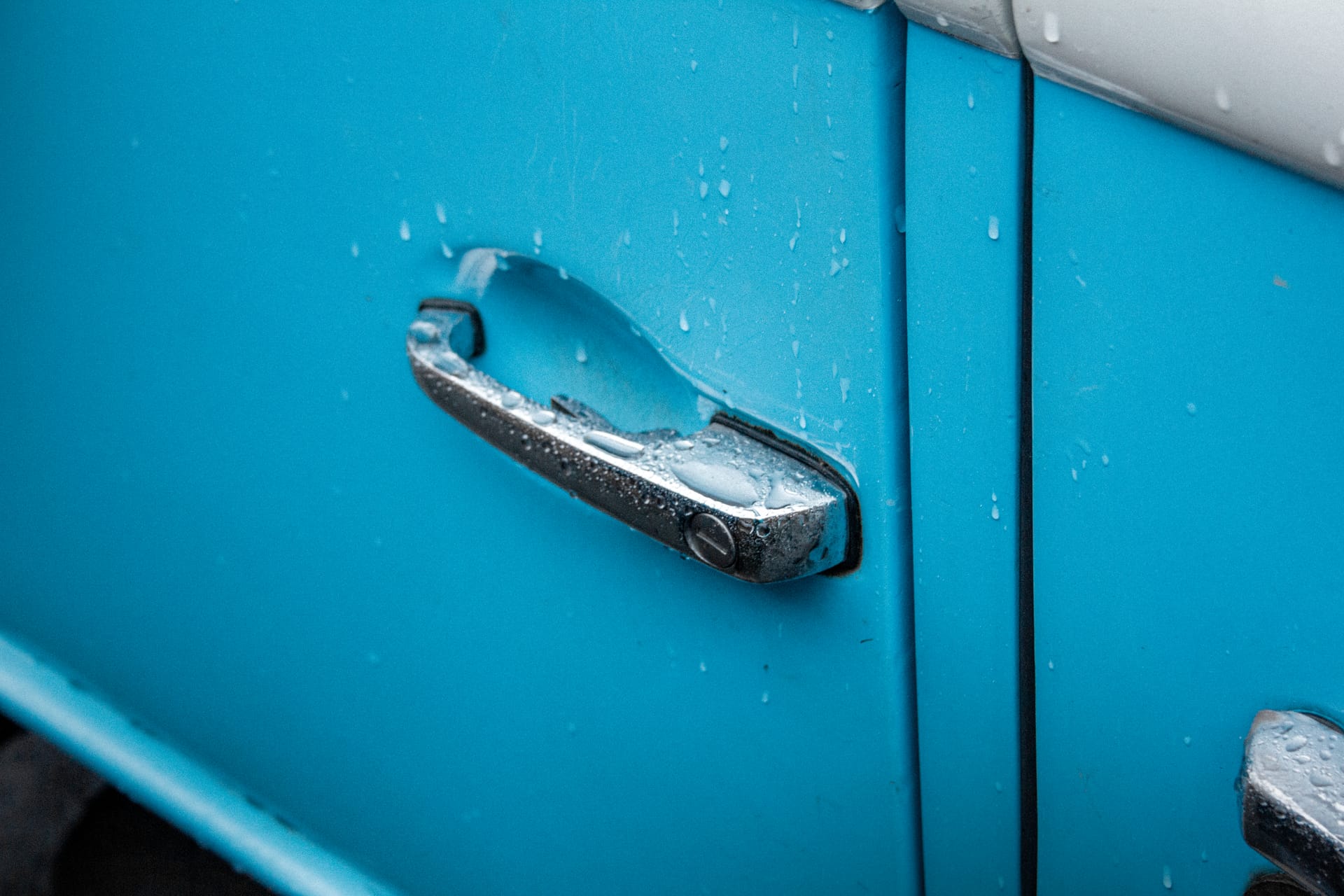 Close-up image of a vintage blue camper van door handle with raindrops, captured outdoors in Shrewsbury, England.